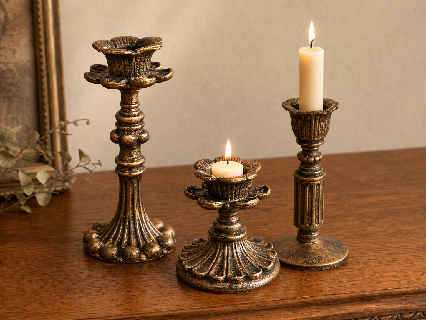 Three antique-bronze taper candle holders at varied heights on a wooden sideboard