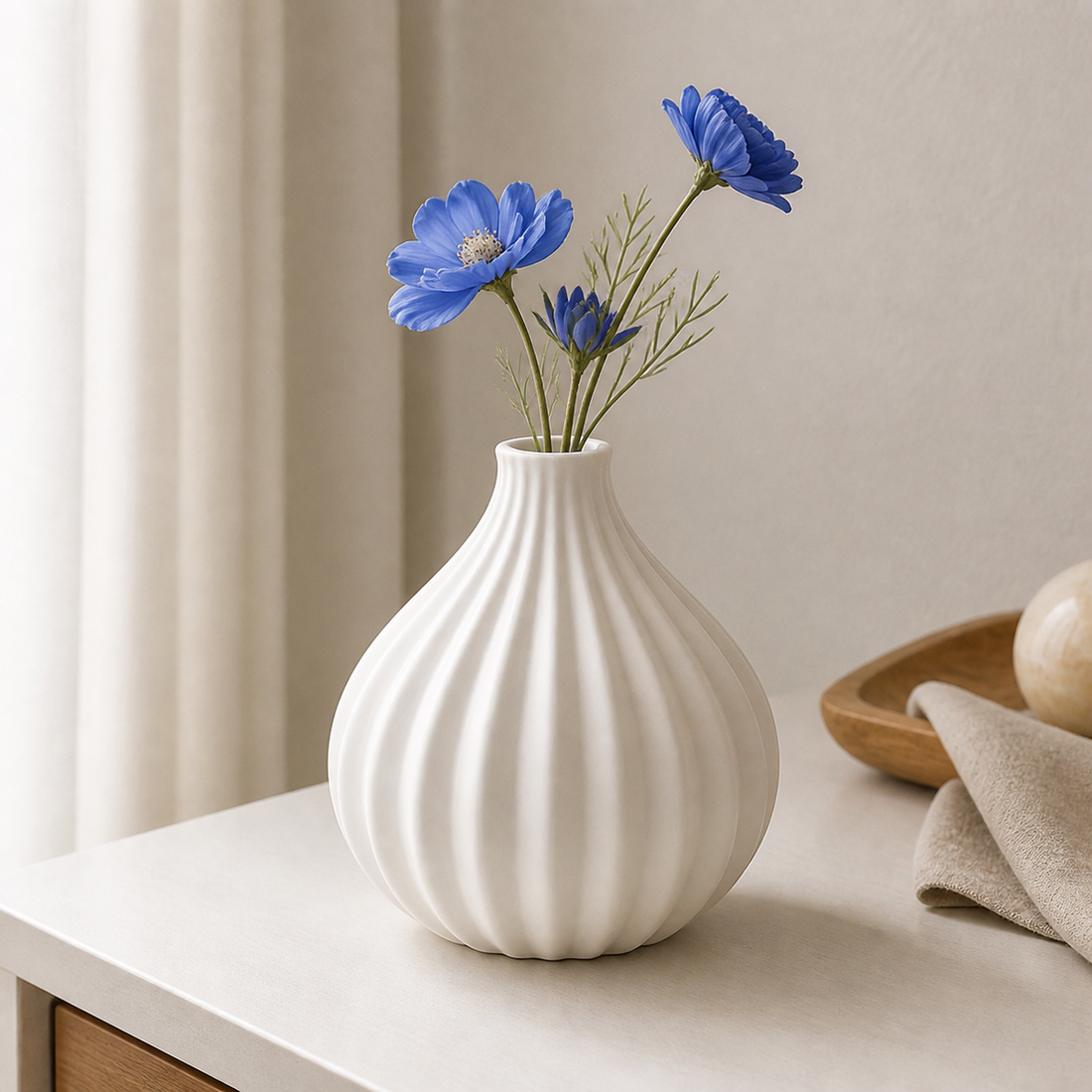White ribbed pumpkin-shaped ceramic vase holding blue cornflowers on a pale console table