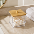 Clear square cotton-swab dispenser with bamboo lid on a warm neutral bathroom vanity