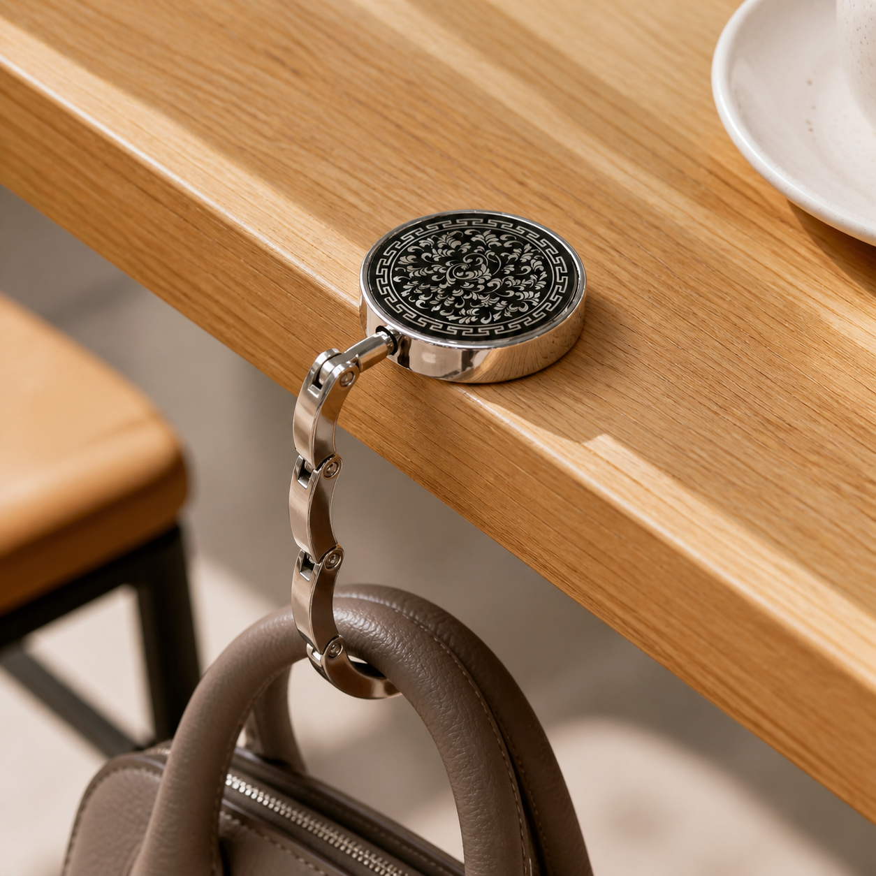 Ornate black floral foldable purse hook open on an oak cafe table with a taupe handbag