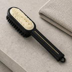 Black two-sided shoe brush showing cream raised grooves black bristles and a thin gold handle accent