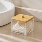 Clear bamboo-lid cotton-swab dispenser beside a white bathroom sink