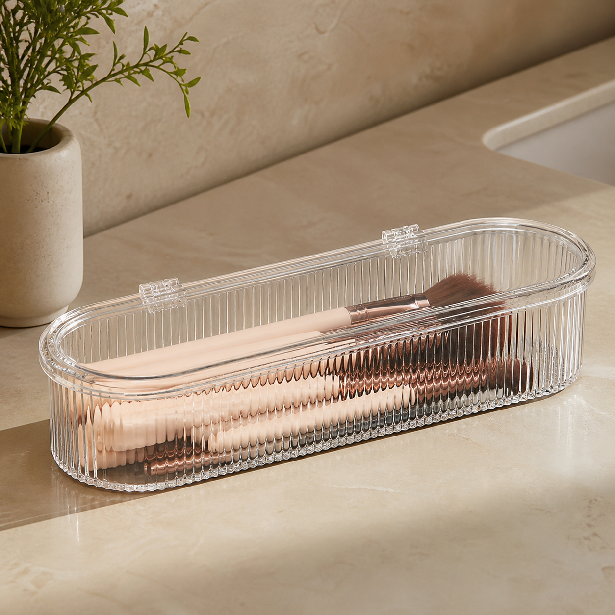 Long clear ribbed makeup brush storage box closed on a neutral bathroom counter