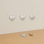 Thin 2 cm frameless silver heart mirror stickers shown beside a small button for scale