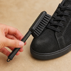 Dense black bristle side of the black suede shoe brush used gently on a black sneaker