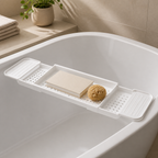 Matte white three-piece bathtub bridge tray styled with a book and bath sponge in a bright bathroom