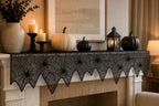 Black spider web table runner layered with pumpkins and candle decor on a mantel