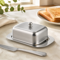 Opaque stainless-steel butter dish with rounded lid and lift knob on a bright kitchen counter