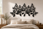 Wide horizontal leaf-branch wall sculpture in matte black, hung above a linen-dressed bed